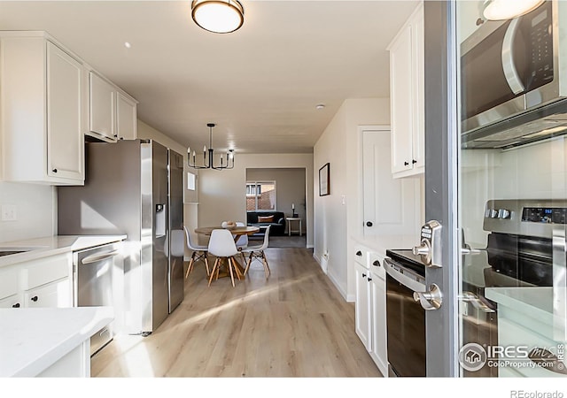 kitchen featuring decorative light fixtures, stainless steel appliances, light countertops, light wood-type flooring, and white cabinetry