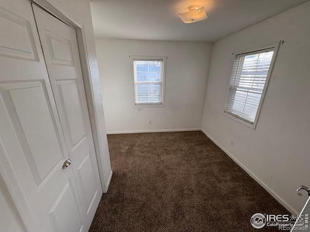 unfurnished bedroom with dark colored carpet and a closet
