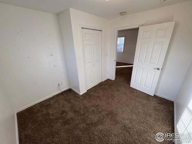 unfurnished bedroom featuring dark carpet and a closet