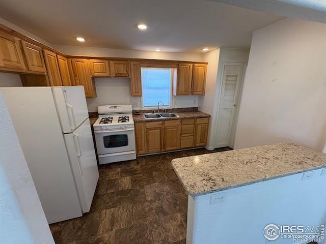 kitchen with white appliances, light stone counters, and sink