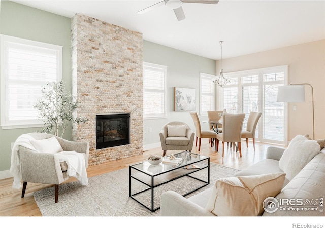 living room featuring ceiling fan with notable chandelier, a stone fireplace, and light wood-type flooring