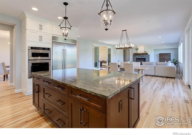 kitchen with a stone fireplace, light hardwood / wood-style flooring, a center island, and appliances with stainless steel finishes