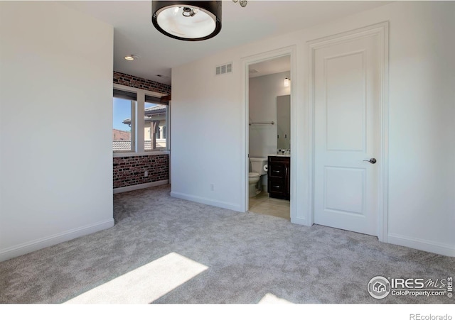 unfurnished bedroom with ensuite bathroom, light colored carpet, and brick wall