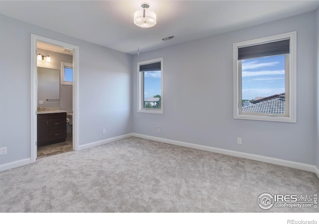 unfurnished bedroom featuring ensuite bathroom, light colored carpet, and sink