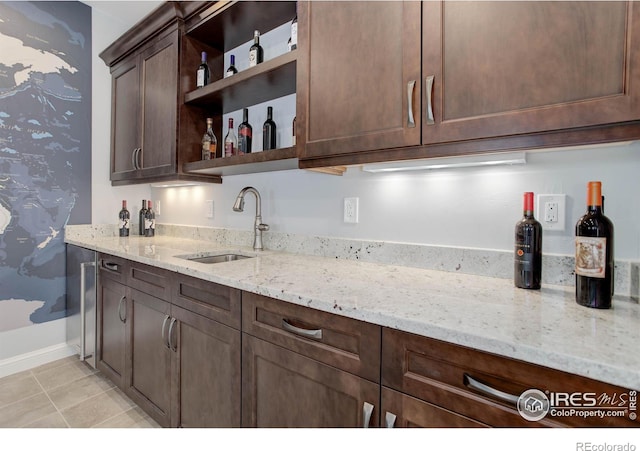 kitchen featuring dark brown cabinetry, light stone counters, sink, and light tile patterned floors