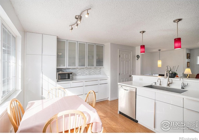 kitchen featuring white cabinetry, sink, stainless steel appliances, decorative light fixtures, and light wood-type flooring