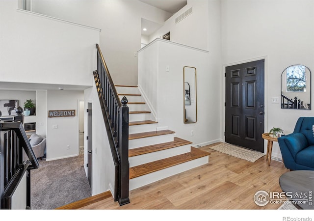 foyer entrance with a towering ceiling, visible vents, stairs, baseboards, and light wood-type flooring