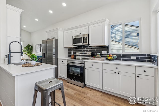 kitchen with stainless steel appliances, a sink, white cabinetry, light wood-type flooring, and decorative backsplash