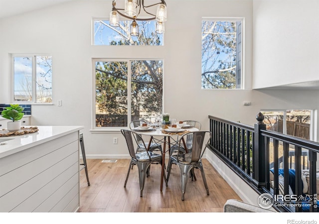 dining room with vaulted ceiling, light wood-style flooring, baseboards, and an inviting chandelier