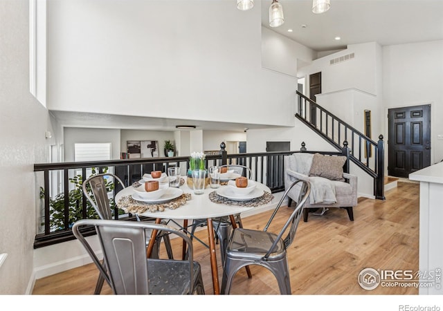 dining space with light wood-type flooring, a high ceiling, and visible vents