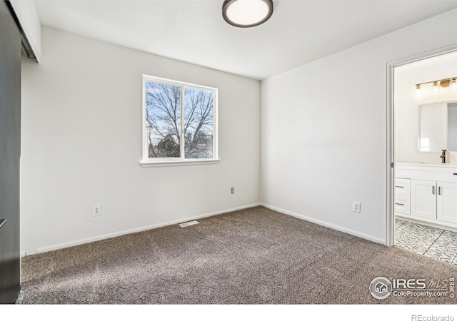 unfurnished bedroom featuring baseboards, visible vents, ensuite bathroom, carpet, and a sink