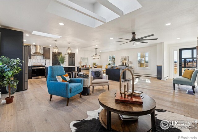 living room with ceiling fan with notable chandelier, light wood-type flooring, baseboard heating, and a skylight