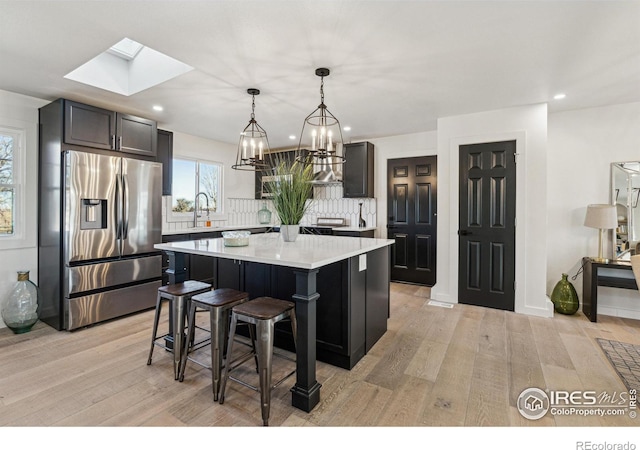 kitchen with stainless steel fridge, a skylight, pendant lighting, a center island, and a breakfast bar area