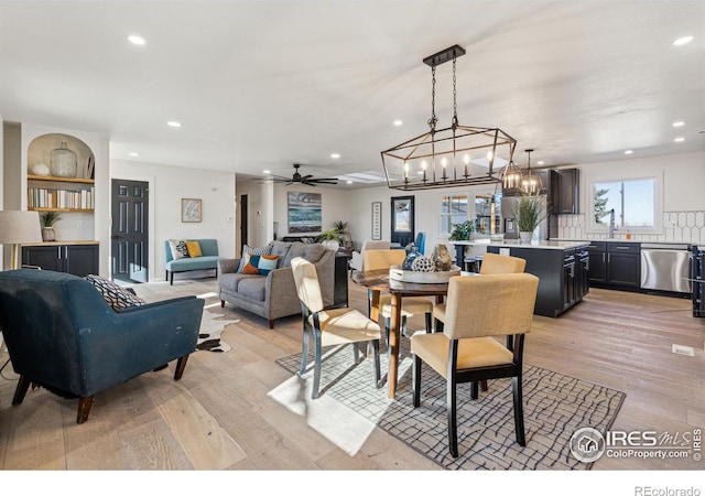 dining room with built in shelves, light hardwood / wood-style floors, and ceiling fan with notable chandelier