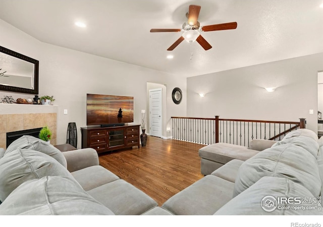 living room featuring ceiling fan, dark wood-type flooring, and a tiled fireplace