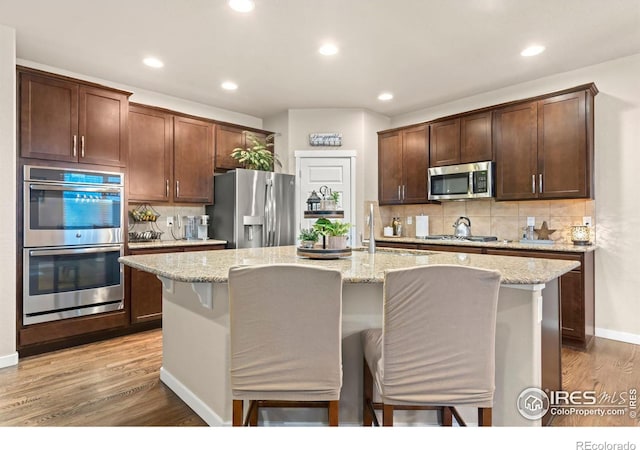 kitchen with a kitchen breakfast bar, light hardwood / wood-style floors, an island with sink, and appliances with stainless steel finishes