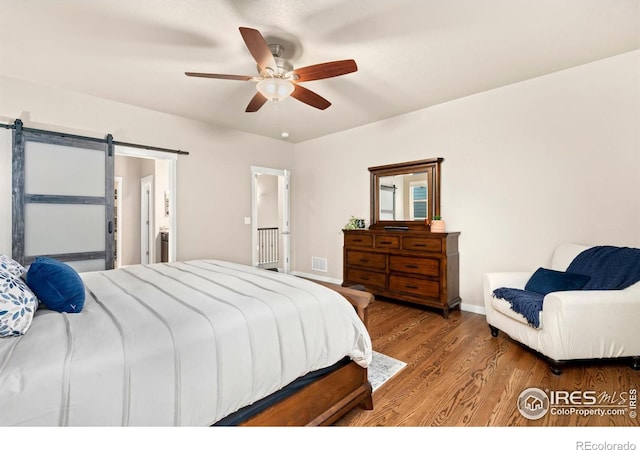 bedroom featuring connected bathroom, ceiling fan, hardwood / wood-style floors, and a barn door