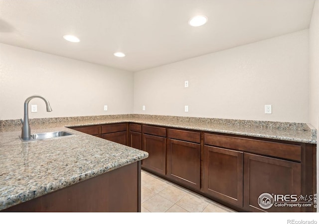 kitchen featuring dark brown cabinets, light stone countertops, sink, and light tile patterned floors