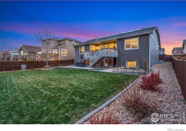 back house at dusk with a lawn, a patio area, and a deck