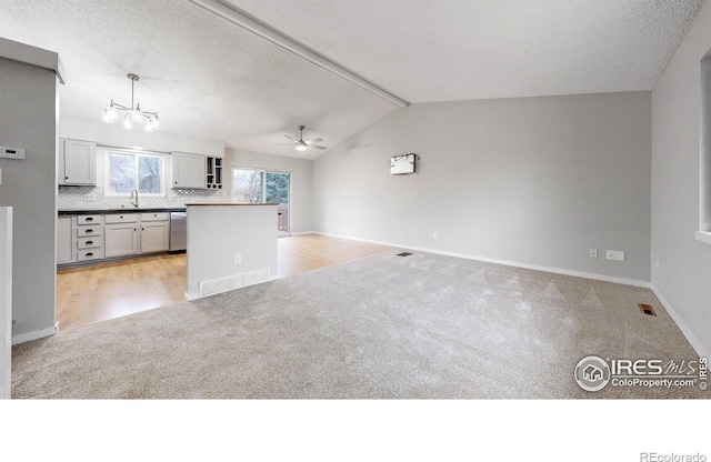 kitchen featuring stainless steel dishwasher, vaulted ceiling, sink, decorative light fixtures, and light hardwood / wood-style floors