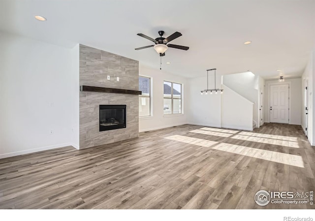 unfurnished living room featuring ceiling fan, a fireplace, wood finished floors, and baseboards