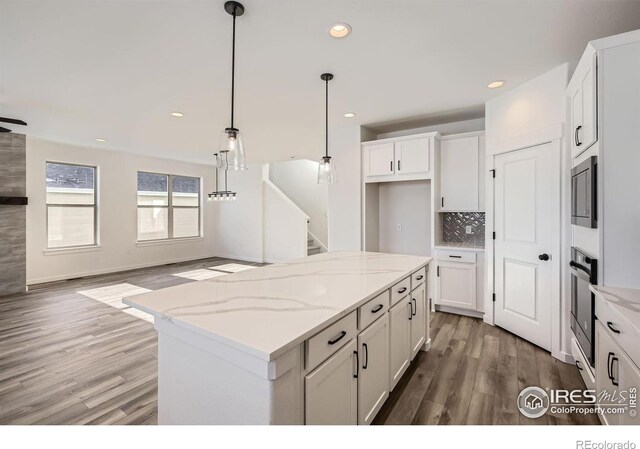 kitchen featuring tasteful backsplash, open floor plan, white cabinets, wood finished floors, and black oven