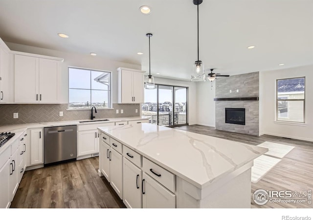 kitchen featuring decorative backsplash, dishwasher, a tile fireplace, a center island, and a sink