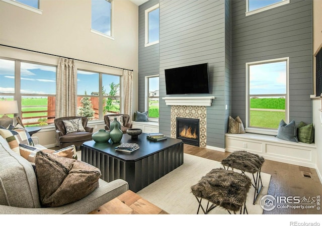 living room featuring hardwood / wood-style flooring, a wealth of natural light, a high ceiling, and a tiled fireplace