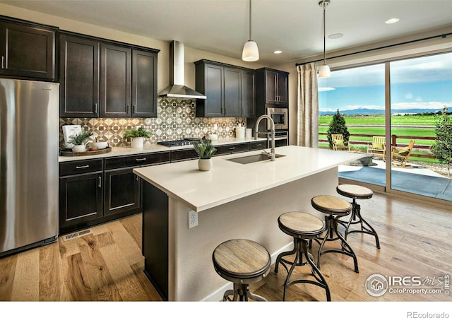 kitchen with sink, wall chimney exhaust hood, stainless steel appliances, decorative light fixtures, and light wood-type flooring