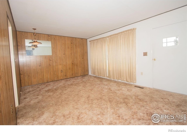 carpeted empty room featuring wooden walls