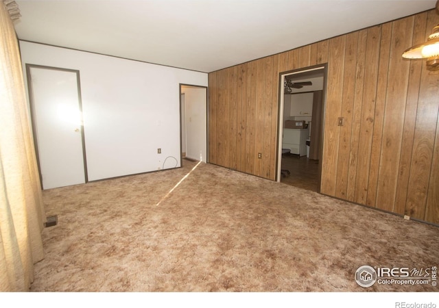 unfurnished bedroom with light carpet, separate washer and dryer, a closet, and wood walls