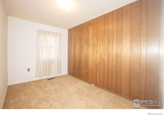 spare room with light carpet and wood walls