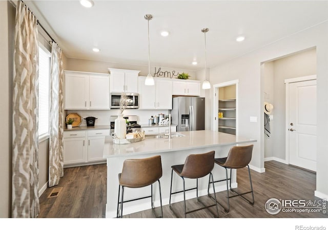 kitchen featuring appliances with stainless steel finishes, decorative light fixtures, white cabinetry, and a center island with sink