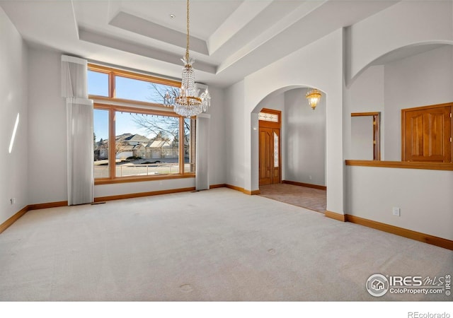 unfurnished room with a raised ceiling, carpet floors, and a chandelier