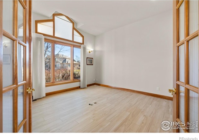 spare room featuring vaulted ceiling, light hardwood / wood-style flooring, and french doors