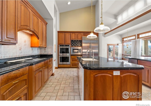 kitchen with backsplash, sink, built in appliances, decorative light fixtures, and a center island with sink