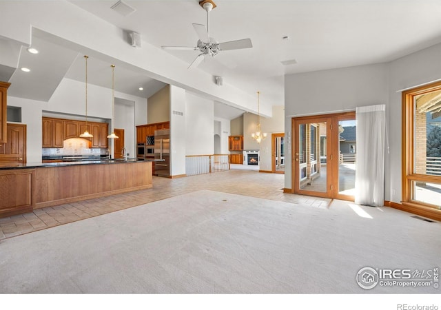 unfurnished living room featuring light carpet, high vaulted ceiling, and ceiling fan with notable chandelier