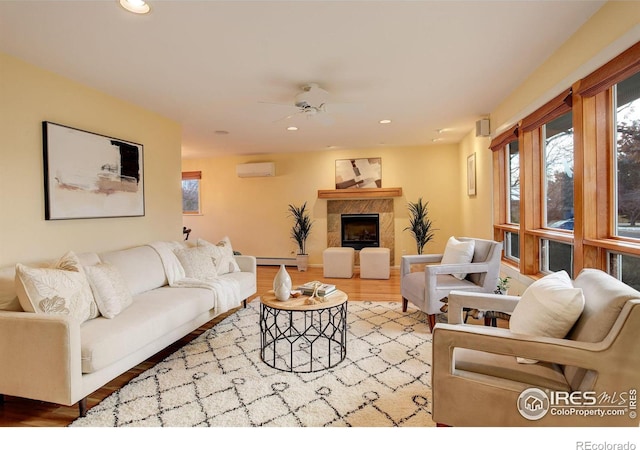 living room with ceiling fan, a wall mounted AC, a baseboard radiator, a premium fireplace, and light hardwood / wood-style floors