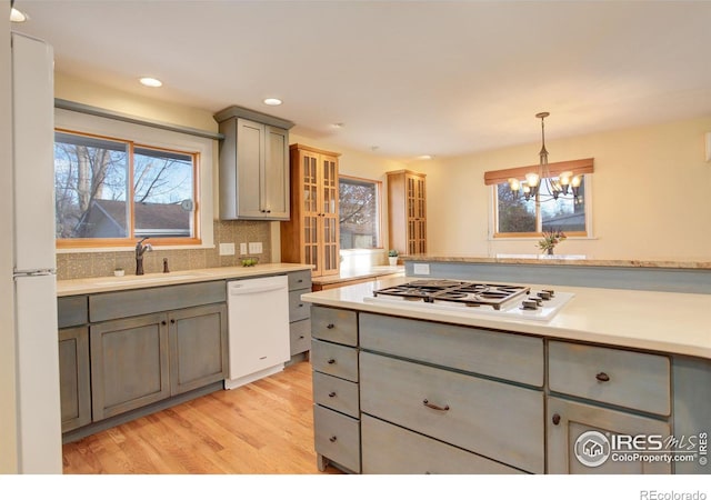 kitchen featuring gray cabinetry, light hardwood / wood-style flooring, a notable chandelier, pendant lighting, and white appliances