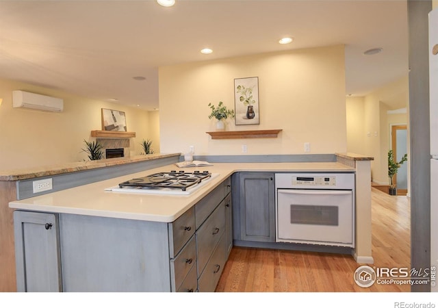 kitchen featuring stainless steel gas cooktop, light hardwood / wood-style flooring, a wall unit AC, kitchen peninsula, and oven