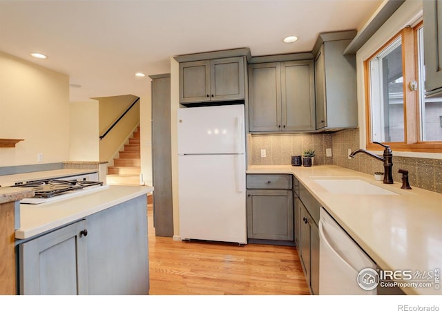 kitchen with tasteful backsplash, gray cabinetry, white appliances, sink, and light hardwood / wood-style flooring