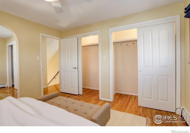 bedroom with hardwood / wood-style flooring, baseboard heating, ceiling fan, and multiple closets