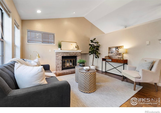 living room featuring wood-type flooring, a brick fireplace, and lofted ceiling