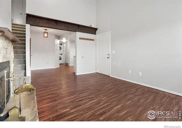 living room with a towering ceiling, a stone fireplace, stacked washer / dryer, and dark wood-type flooring