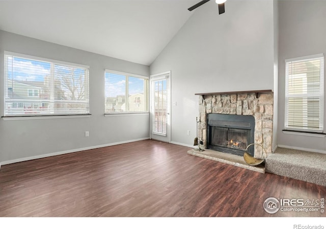 unfurnished living room with dark hardwood / wood-style floors, ceiling fan, a stone fireplace, and high vaulted ceiling