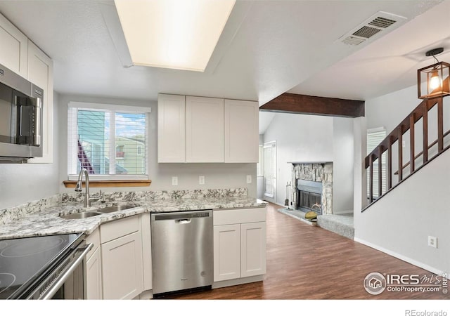 kitchen featuring a stone fireplace, sink, dark hardwood / wood-style floors, appliances with stainless steel finishes, and white cabinetry