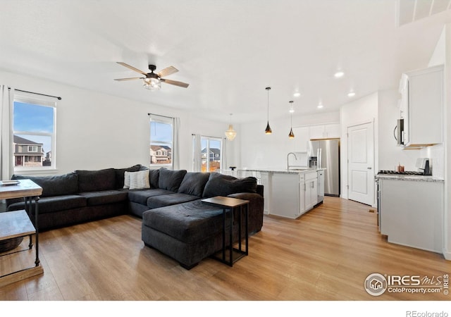 living room with ceiling fan, plenty of natural light, sink, and light hardwood / wood-style flooring