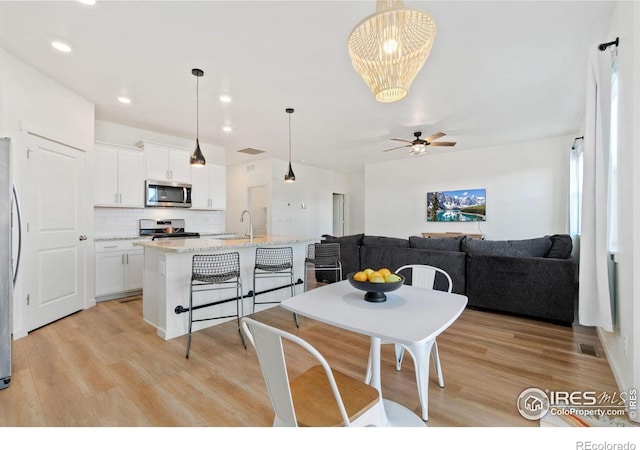 dining space with sink, light hardwood / wood-style floors, and ceiling fan with notable chandelier