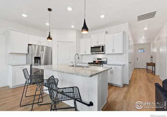 kitchen featuring pendant lighting, a kitchen island with sink, light wood-type flooring, white cabinetry, and stainless steel appliances