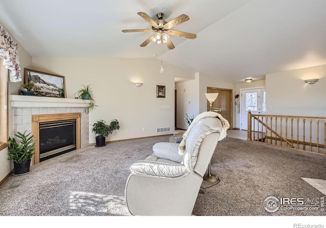 carpeted living room featuring a tiled fireplace, vaulted ceiling, and ceiling fan